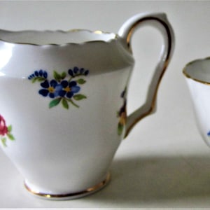 May include: A white porcelain creamer and sugar bowl set with a floral pattern. The creamer has a scalloped edge and a handle. The sugar bowl has a round shape and a gold rim.