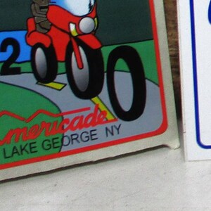 May include: Six embroidered patches featuring the text "Americade" and "World's Largest Motorcycle Touring Rally". The patches are white with blue and red accents. One patch features a map of the United States with the text "20 years".