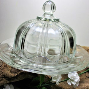 May include: A clear glass butter dish with a fluted dome lid and a scalloped edge plate.
