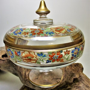 May include: A clear glass candy dish with a gold rim and floral design. The dish has a lid with a gold finial.