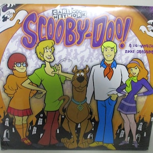 May include: A 16-month 2002 calendar featuring the Scooby-Doo cartoon characters. The calendar shows the characters: Fred, Daphne, Velma, Shaggy, and Scooby-Doo. The background is orange with a purple Scooby-Doo logo and white ghosts.