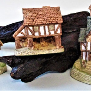May include: Three miniature houses with brown, green, and gray roofs, each with white trim and a wooden front porch. The houses are displayed on a dark brown wooden base.