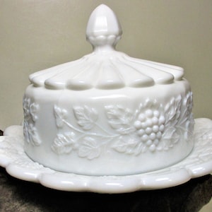 May include: White milk glass butter dish with a domed lid and a scalloped base. The lid and base are decorated with a raised design of grapes and leaves.