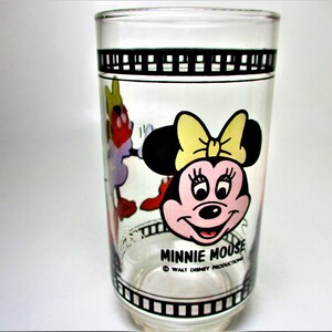 May include: A clear glass drinking glass with a black and white film strip design around the top and bottom. The glass features a colourful cartoon image of Minnie Mouse with the text "Minnie Mouse" and "&copy; WALT DISNEY PRODUCTIONS".