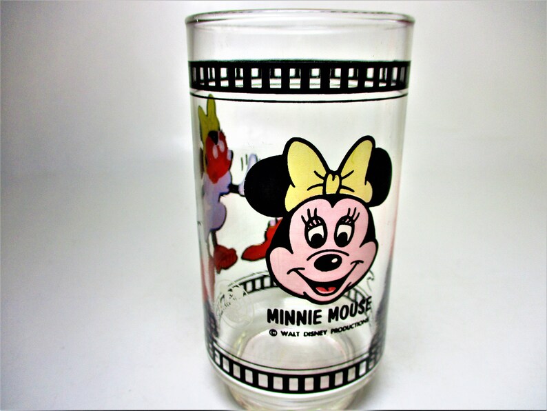 May include: A clear glass drinking glass with a black and white film strip design around the top and bottom. The glass features a colourful cartoon image of Minnie Mouse with the text "Minnie Mouse" and "&copy; WALT DISNEY PRODUCTIONS".