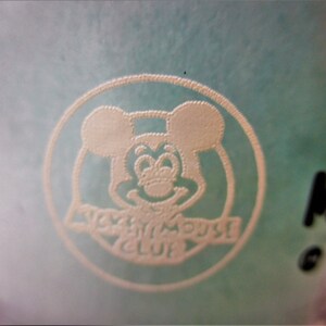 May include: A white Mickey Mouse head logo with the text "Disney Movie Club" on a light blue background.
