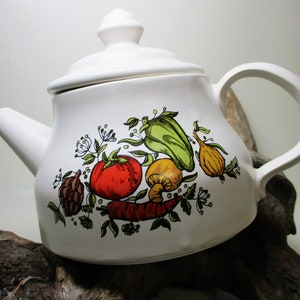May include: White ceramic teapot with a lid and a handle. The teapot has a colorful vegetable design with a red tomato, green pepper, yellow onion, and brown mushrooms.