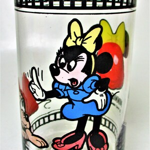 May include: A clear glass drinking glass with a black and white film strip design around the top and bottom. The glass features a cartoon image of Minnie Mouse in a blue dress with a yellow bow, and a red and white cartoon image of Mickey Mouse.