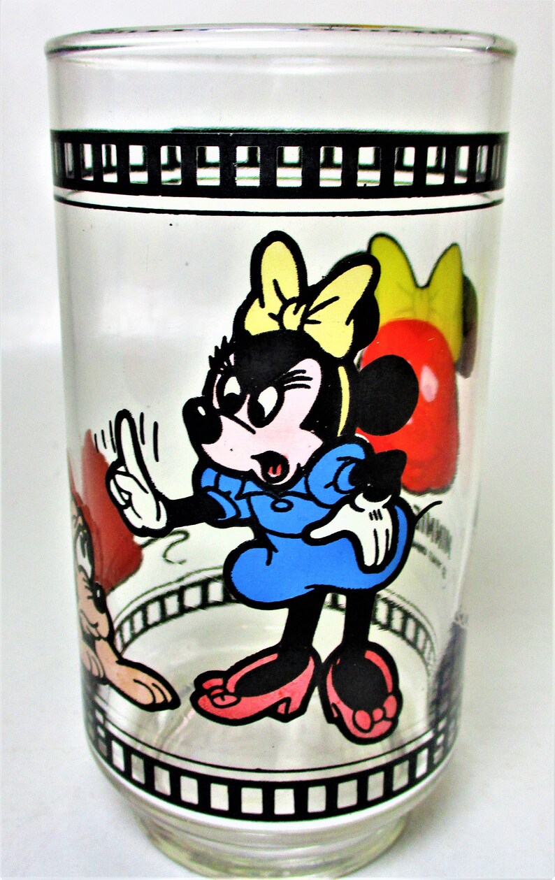 May include: A clear glass drinking glass with a black and white film strip design around the top and bottom. The glass features a cartoon image of Minnie Mouse in a blue dress with a yellow bow, and a red and white cartoon image of Mickey Mouse.