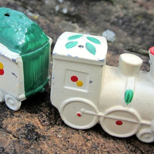 May include: A white toy train with green and red accents. The train has a boxcar with a green roof and a locomotive with green leaves on the top.
