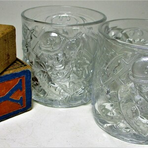 May include: Two clear glass mugs with a raised design of the Riddler from Batman. The mugs are next to three wooden alphabet blocks that spell "A Y B".