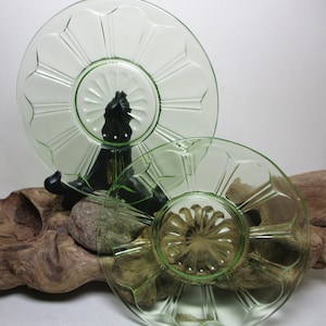 May include: Two green glass plates with a scalloped edge and a floral design. The plates are on a wooden stand.