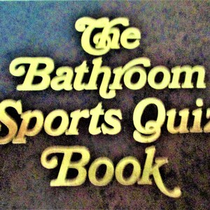 May include: The Bathroom Sports Quiz Book, a book title in gold lettering on a dark brown background.