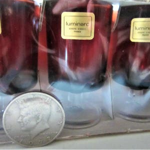 May include: Set of four clear glass stemmed wine glasses with a red tint. The glasses are packaged in a clear plastic box. The box has a label that reads "luminarc verres a vin rouge France".