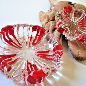 May include: Two clear glass ashtrays with red and white swirl designs. The ashtrays are shaped like a flower with a deep center.