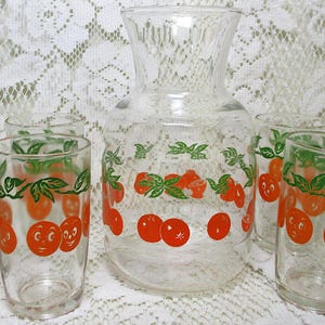 May include: A vintage clear glass pitcher and six matching glasses. The pitcher and glasses are decorated with orange smiling fruit and green leaves. A charming retro drinkware set.