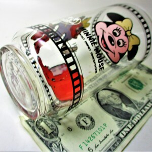 May include: A clear glass drinking glass with a black and white film strip design and a cartoon image of Minnie Mouse. The glass has the text "Minnie Mouse" and "Walt Disney Productions" printed on it.