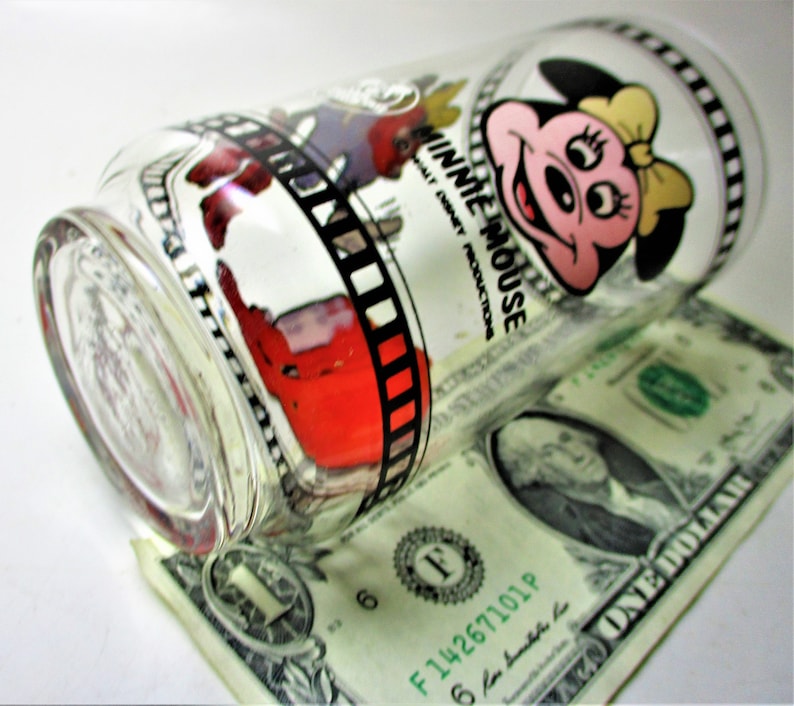 May include: A clear glass drinking glass with a black and white film strip design and a cartoon image of Minnie Mouse. The glass has the text "Minnie Mouse" and "Walt Disney Productions" printed on it.
