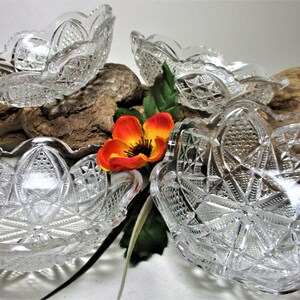 May include: Four clear glass bowls with a cut glass design. The bowls are arranged on a piece of driftwood with a single orange flower.