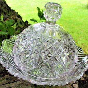 May include: A clear glass butter dish with a scalloped edge and a domed lid. The dish and lid are decorated with a cut glass pattern.