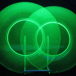 May include: Three green glass plates with a decorative etched design. The plates are stacked on top of each other and are illuminated from behind, creating a glowing effect.