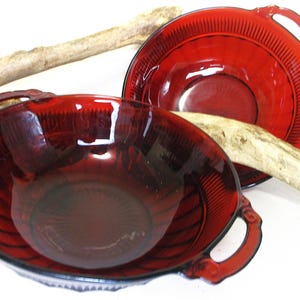 May include: Two red glass bowls with handles. The bowls have a ribbed design and are made of ruby red glass.