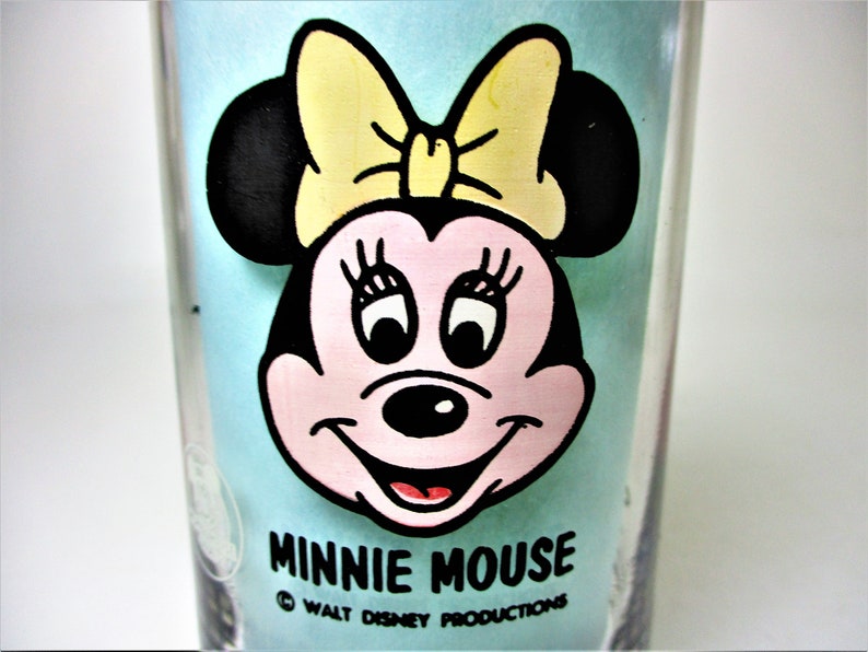 May include: A blue glass featuring a cartoon image of Minnie Mouse wearing a yellow bow. The text "Minnie Mouse" and "Walt Disney Productions" is printed below the image.