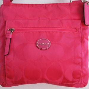 May include: A pink Coach crossbody bag with a silver logo and a zippered pocket. The bag has a signature C pattern.