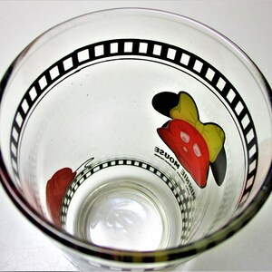 May include: A clear glass drinking glass with a black and white film strip design around the rim. The glass features a red and yellow cartoon image of Minnie Mouse with the text "Minnie Mouse" printed on the glass.