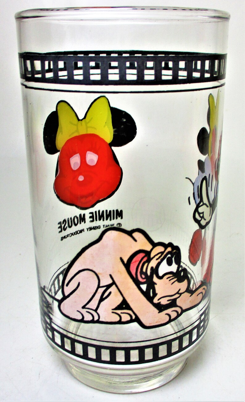 May include: A clear glass drinking glass with a black and white film strip design around the top and bottom. The glass features cartoon images of Mickey Mouse, Minnie Mouse, and Pluto. The text "Minnie Mouse" is printed on the glass.