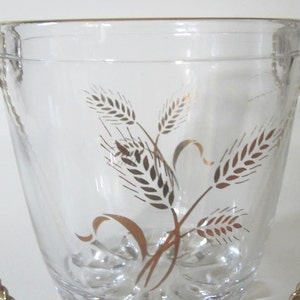 May include: A clear glass ice bucket with a gold rope handle and a gold wheat design.