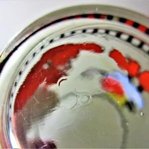 May include: Close-up of the base of a clear glass with a red, white and blue design. The glass has a black and white chequered band around the rim.
