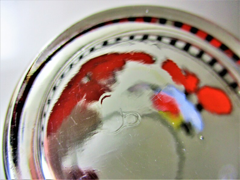 May include: Close-up of the base of a clear glass with a red, white and blue design. The glass has a black and white chequered band around the rim.