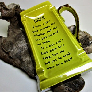 May include: A green ceramic ashtray shaped like a beer stein with a gold handle. The ashtray has a humorous inscription that reads: "BEER I have a few good reasons for drinking, and one has just entered my head. If a man can't drink when he's living, how the hell can he drink when he's dead?"