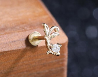 May include: A gold stud earring featuring a delicate, curved vine-like design with a single small, clear round gemstone set at the tip. The metal has a polished finish, and the post is visible extending from the back of the decorative element.