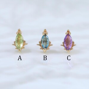 May include: Three gold-colored stud earrings, each with a different colored gemstone. The gemstones are green, blue, and purple. Each earring is labeled with a letter: A, B, and C.