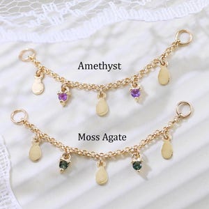 May include: Two gold-coloured chain jewellery pieces. The top piece is labelled "Amethyst" and features purple gemstones and teardrop-shaped charms. The bottom piece, labelled "Moss Agate," has green gemstones and similar charms.