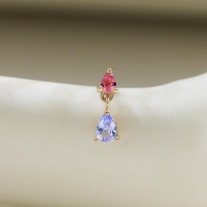 May include: A gold earring featuring a small round pink gemstone set above a dangling pear-shaped light blue gemstone. The piece is constructed with a delicate gold metal setting that connects the two stones in a vertical drop design.