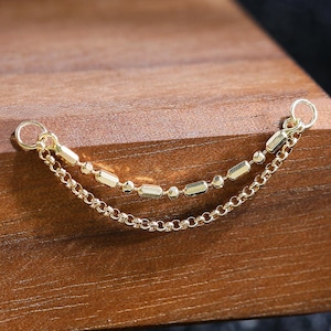 Peut inclure: Un connecteur de chaîne double doré composé d'une fine chaîne maille forçat associée à une seconde chaîne ornée de petites perles cylindriques allongées. Chaque extrémité de l'assemblage de chaînes se termine par un petit anneau de jonction.