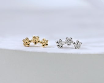 May include: Two dainty flower-shaped earrings, one in gold and one in silver, are displayed on a white surface. The earrings are made of small, round beads that are clustered together to form the shape of a flower.