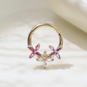 May include: A gold-colored hinged ring earring with three flower clusters. Each cluster features pink and white gemstones. The earring is designed for a piercing and is set against a white background.