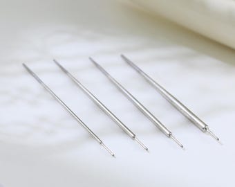 May include: Four silver metal tools with pointed tips are arranged diagonally on a white surface. The tools are of varying lengths, with a curved white object in the background. The tools appear to be for a craft or hobby.