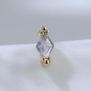 Könnte beinhalten: Ein kleiner, goldfarbener Ohrring mit einem rautenförmigen, irisierenden Edelstein. Der Ohrring hat dekorative Elemente oben und unten, vor weißem Hintergrund.