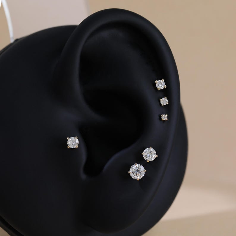 Puede incluir: Un conjunto de seis pendientes de bot&oacute;n redondos, transparentes y de talla brillante con engastes dorados, dispuestos en grupo a lo largo de la curva de un modelo de exhibici&oacute;n negro con forma de oreja. Los pendientes var&iacute;an en tama&ntilde;o.