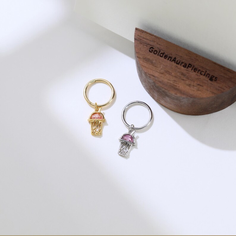 Peut inclure: Deux boucles d'oreilles cr&eacute;oles avec un charme de panier de basket-ball. Les cr&eacute;oles sont en or et en argent. Les charmes de panier de basket-ball ont un bijou rose et un bijou transparent au centre.