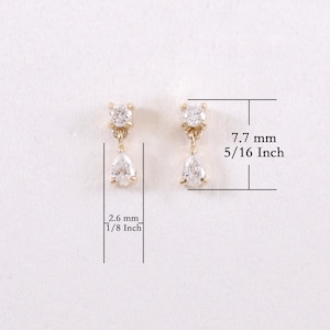 May include: A pair of gold-toned earrings with a small, square-shaped top and a pear-shaped drop. The earrings are 5/16 inch (7.7 mm) long and 1/8 inch (2.6 mm) wide. The earrings are set against a white background.