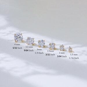 Puede incluir: Seis pendientes de bot&oacute;n dorados con piedras redondas transparentes, ordenados por tama&ntilde;o desde 4 mm hasta 1,5 mm. Cada pendiente presenta un engaste de cuatro garras que sujeta una piedra facetada, dispuestos en fila con sus medidas.