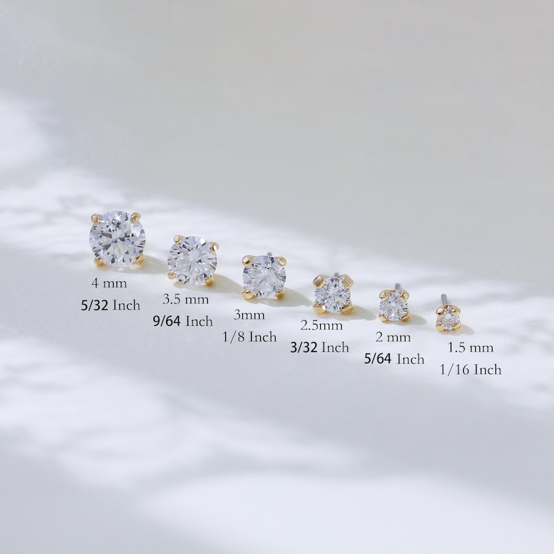 Puede incluir: Seis pendientes de bot&oacute;n dorados con piedras redondas transparentes, ordenados por tama&ntilde;o desde 4 mm hasta 1,5 mm. Cada pendiente presenta un engaste de cuatro garras que sujeta una piedra facetada, dispuestos en fila con sus medidas.