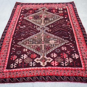 May include: A rectangular, hand-woven rug with a deep burgundy field and intricate geometric patterns in shades of red, brown, and beige. The rug features a detailed border with repeating designs, adding to its traditional aesthetic.