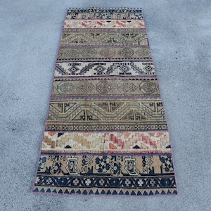 May include: A rectangular, patterned rug with a variety of geometric designs in shades of beige, brown, blue, and red. The rug features a series of horizontal bands with different patterns, creating a textured appearance. The rug is likely made of woven fabric.